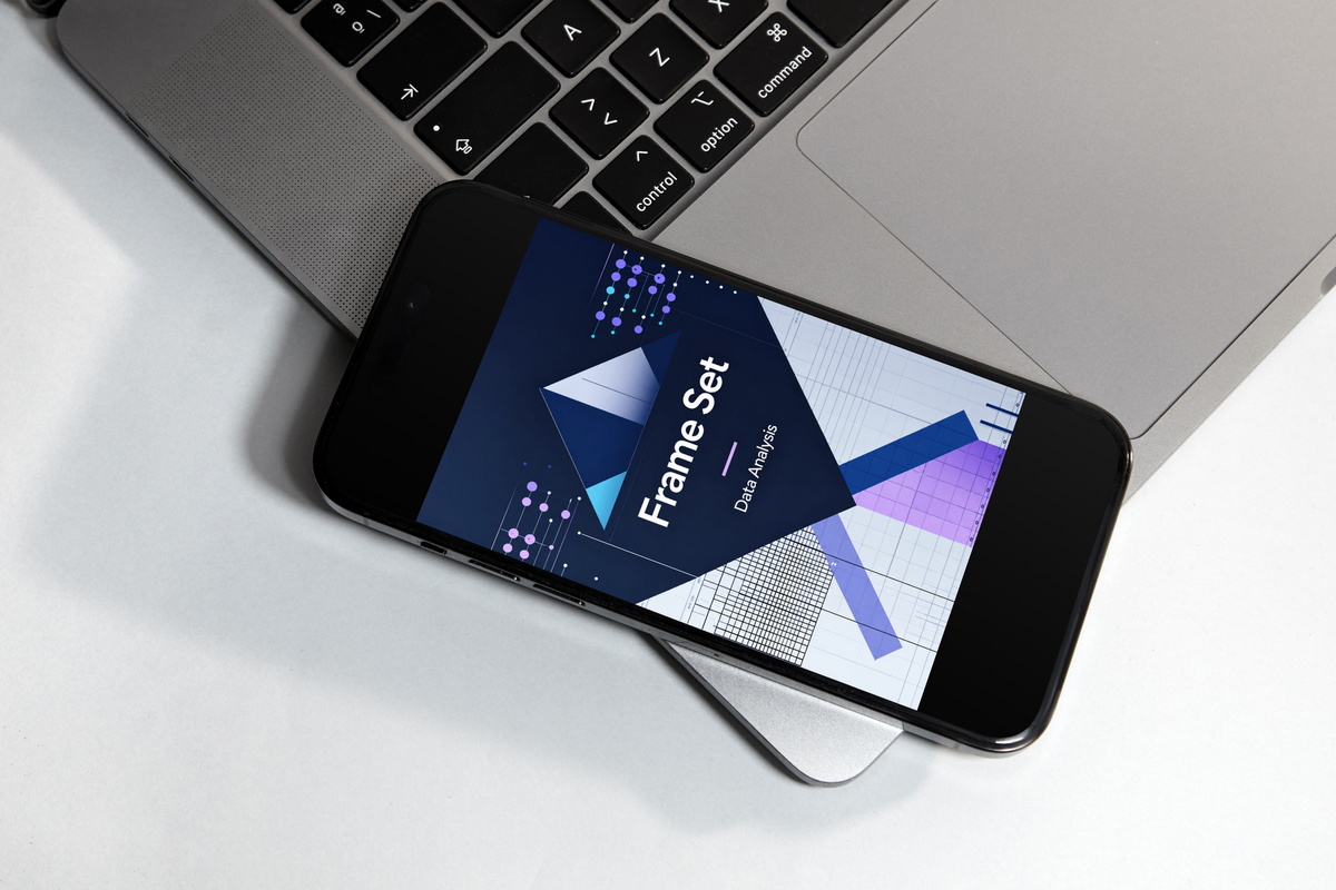 A black smartphone lying diagonally on top of a silver laptop, displaying a dark-themed graphic design template titled 'Frame Set' on its screen.